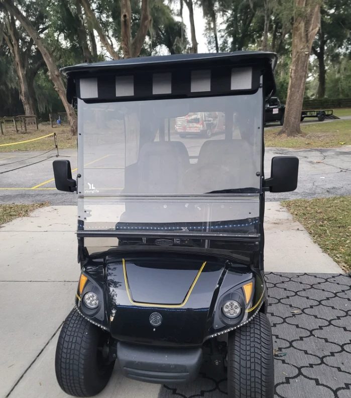 Black and yellow golf cart with enclosed passenger cabin viewed from rear angle
